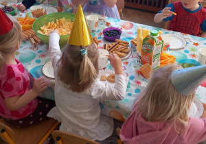 Dzieci siedzą przy stoliku z poczęstunkiem