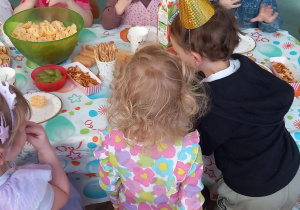 Dzieci siedzą w urodzinowych czapeczkach przy stole i świętują urodziny