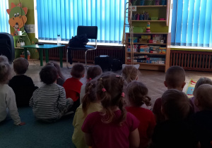 Dzieci siedzą na dywanie i słuchają zagadek