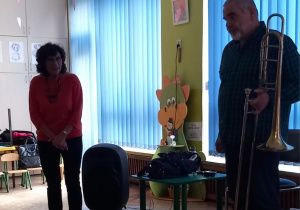 Dzieci siedzą na dywanie i przyglądają się instrumentowi