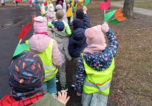 Dzieci idą w parach machając kolorowymi kwiatami z papieru