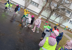 Dzieci idą w parach machając kolorowymi kwiatami z papieru