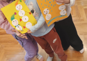 Dzieci trzymają pracę plastyczną z wyklejonymi bałwankami.