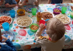 Dzieci siedzą przy stolikach i jedzą łakocie
