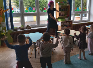 Dzieci stoją naprzeciwko prowadzącej i machają rękoma