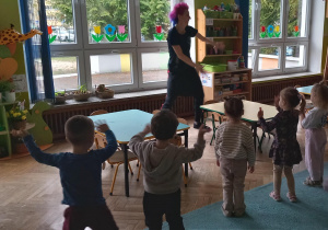 Dzieci stoją naprzeciwko prowadzącej i machają rękoma