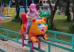 Dziecko jedzie na pomarańczowym zwierzaczku.