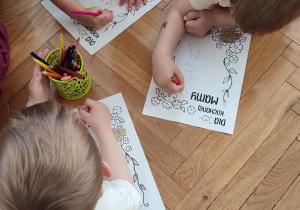 Dzieci leżą na podłodze i kolorują laurkę dla mamy.
