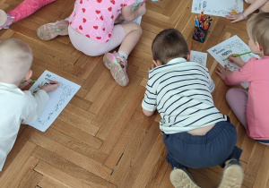 Dzieci leżą na podłodze i kolorują laurkę dla mamy.