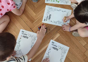 Dzieci leżą na podłodze i kolorują laurkę dla mamy.