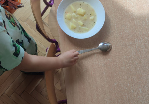 Na stole stoją talerze z zupą. Dziecko obok talerza kładzie łyżkę.