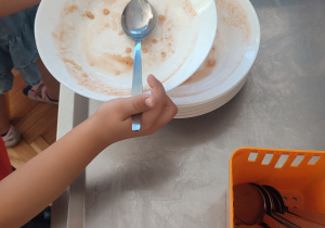 Dziecko odstawia pusty talerz po zupie na kuchenny wózek.