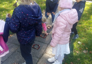 Dzieci w ogrodzie układają koła z kasztanów