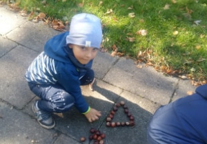 Dzieci układają na chodniku trójkąty z kasztanów