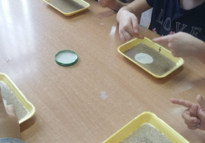 Dzieci przy stoliku wykonują eksperyment z wodą i pieprzem