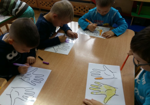 Dzieci przy stoliku kolorują mazakami obrazek dłoni
