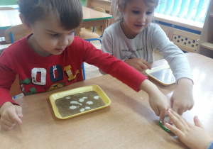 Dzieci przy stoliku brudzą palce wykonując eksperyment