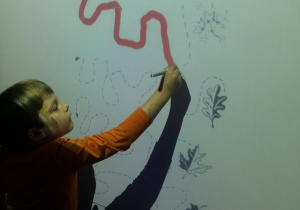 Chłopiec rysuje pisakiem szlaczki na tablicy interaktywnej