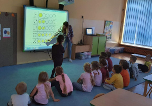 Pani przy tablicy interaktywnej tłumaczy dzieciom wykonanie matematycznego zadania