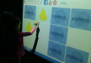 Dziewczynka szuka pary owoców na tablicy interaktywnej