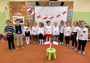 Dzieci w strojach galowych stoją na baczność i śpiewają Hymn Polski