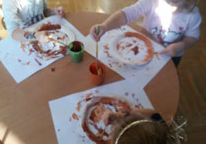 Dzieci malują farbami talerzyki na brązowo
