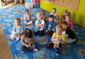 Dzieci siedzą na dywanie ze swoimi pluszowymi przyjaciółmi
