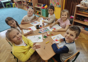Dzieci siedząc przy stoliku kolorują i wyklejają plasteliną misie